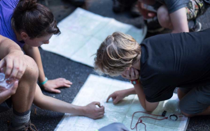 Two students point at a map that is laid out on the ground. 